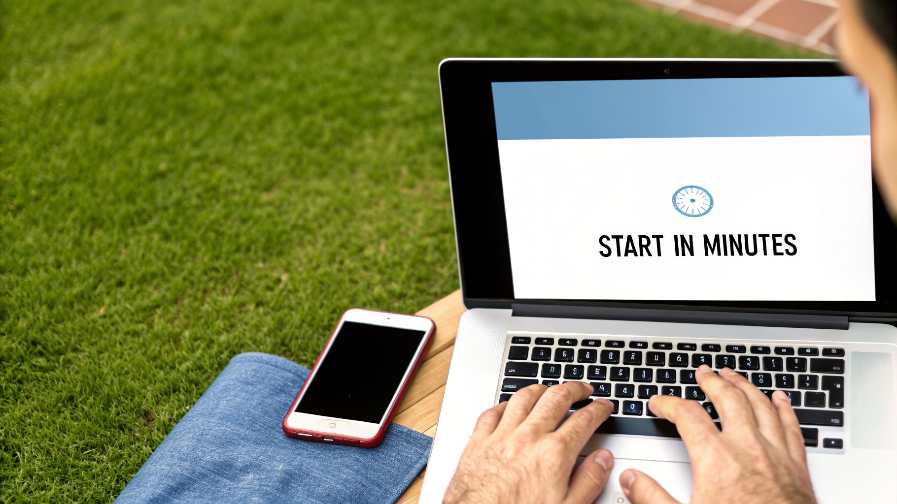 Person typing on a laptop with 'START IN MINUTES' on screen, smartphone next to them outdoors.